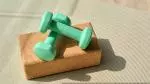 Two green dumb-bells on top of a yoga block on a yoga mat