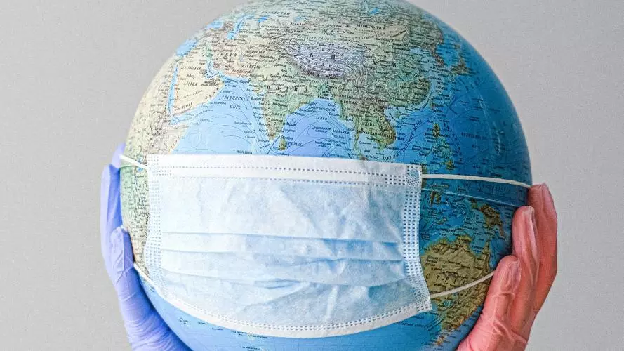 Globe wearing a facemask, being held by hands with medical gloves on.