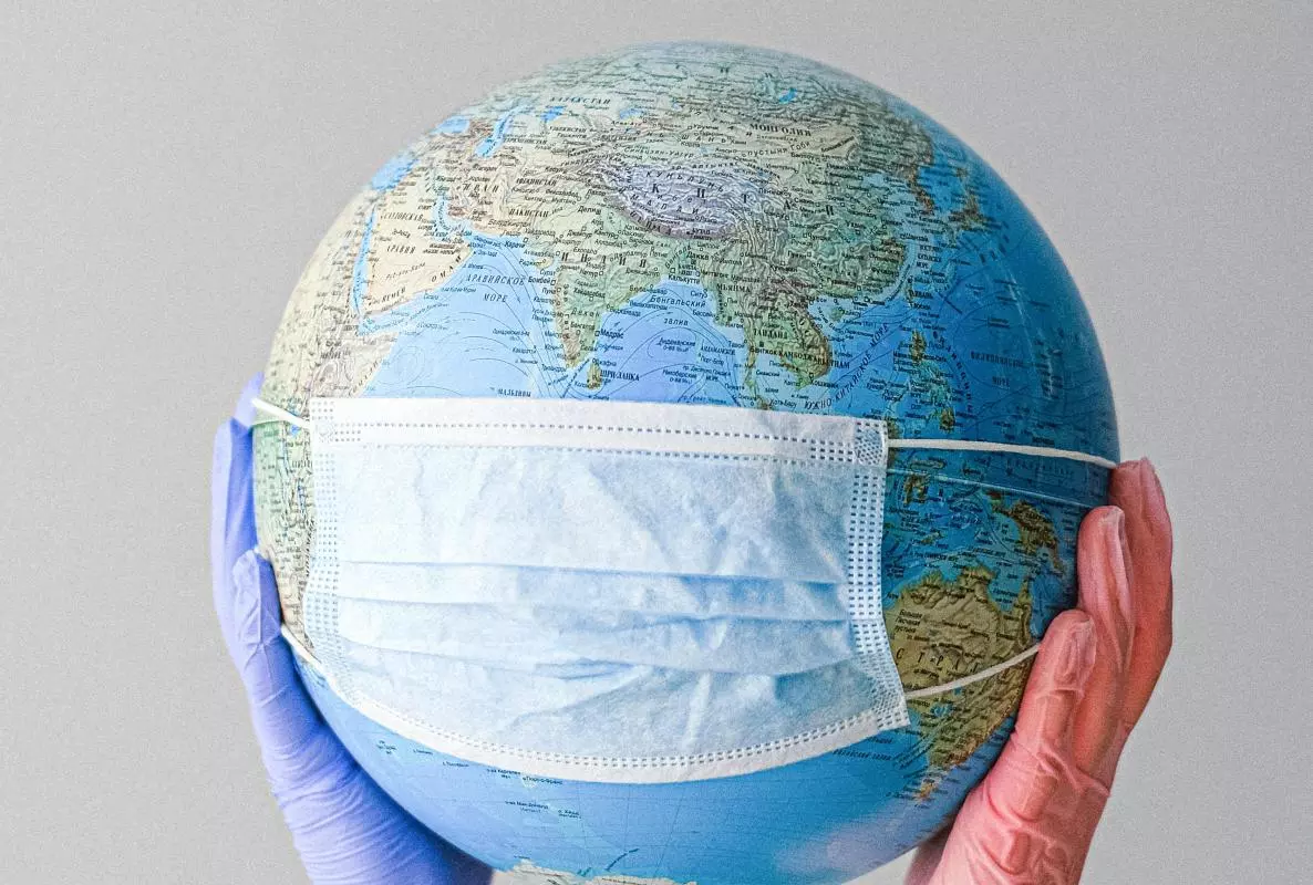 Globe wearing a facemask, being held by hands with medical gloves on.