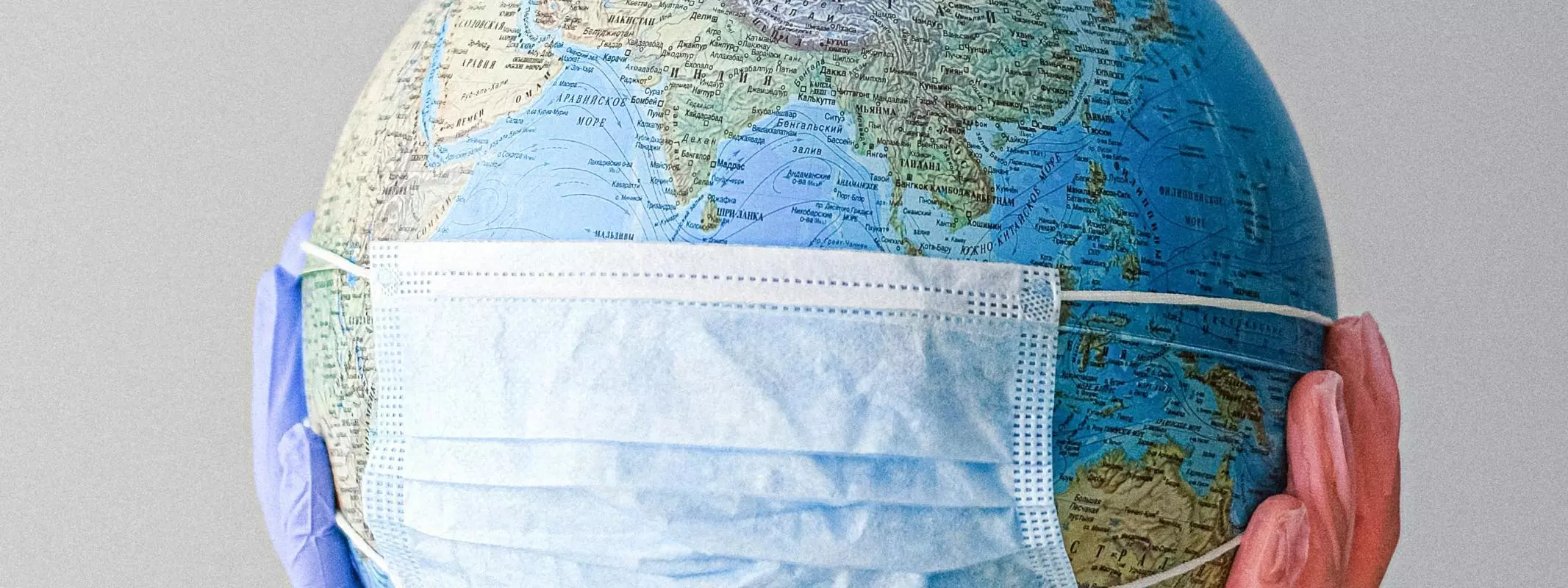 Globe wearing a facemask, being held by hands with medical gloves on.